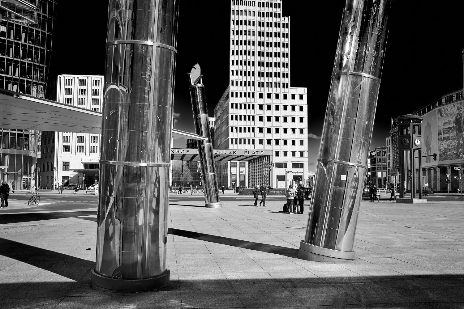 Black and white photograph of Potsdamer Platz in Berlin with large cylindrical metal columns in fore
